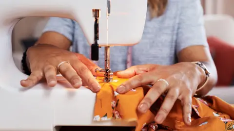 Getty Images Stock image of a woman using a sewing machine to repair a colourful item of clothing