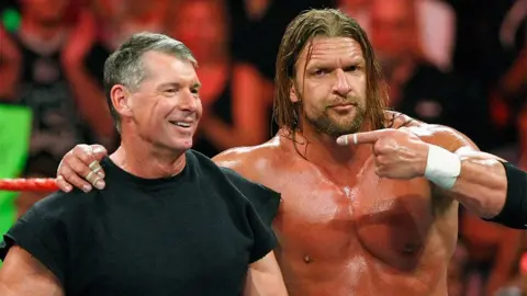 Getty Images Vince McMahon and Triple, standing in the ring, with Triple H pointing towards Vince. There is a full crowd behind them.