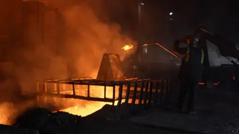 BBC A steelworker at Blast Furnace 4 tests the liquid iron that glows orange as it emerges from the furnace