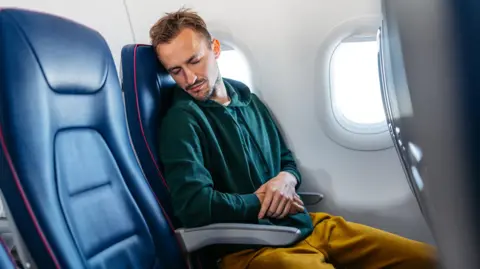 Getty Images Man asleep on plane with both arms on armrests