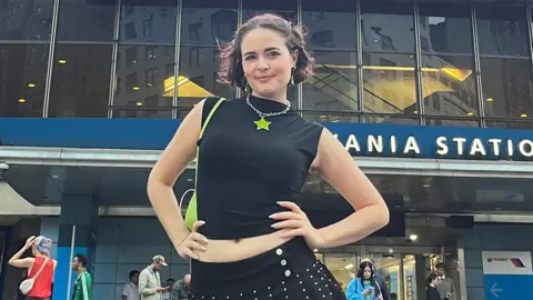 Kelley Heyer Kelley Heyer, a woman, outside Madison Square Gardens, wearing a black top with a lime green star shaped necklace. Her hands are on her hips, with other concert-goers in the background.