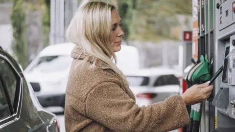 Getty Images A woman pays for fuel at a pump in a petrol station