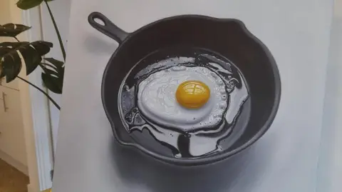 Daniel Halksworth An oil painting of a fried egg in a black skillet. The egg looks in the process of being fried, there are no brown edges yet, only some air bubbles on the right corner as it sits in a sheen of oil.