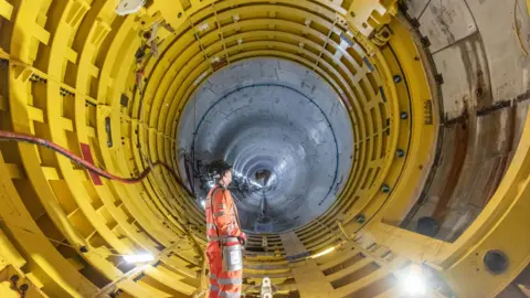 EDF A worker stands in a six metre wide yellow tunnel which stretches away into the distance. It is one of several under the Bristol Channel at Hinkley Point C