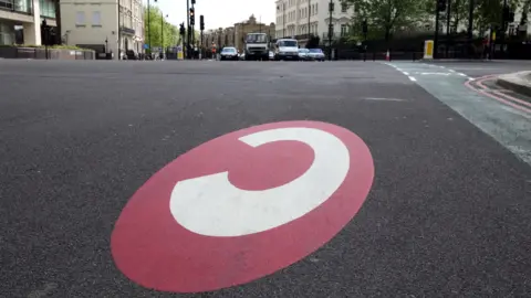 BBC Congestion charge zone marking - a white 'c' on a red circle painted on a road in London 