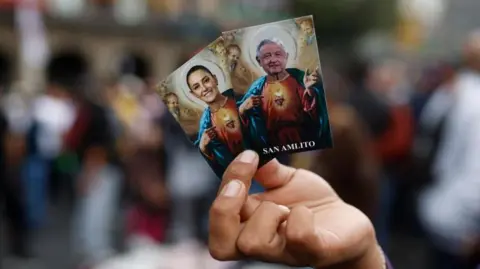 EPA A person holds two cards with the images of Mexico's President Claudia Sheinbaum (L) and former Mexican President Andres Manuel Lopez Obrador, in Mexico City's Zocalo, Mexico, 01 October 2024.