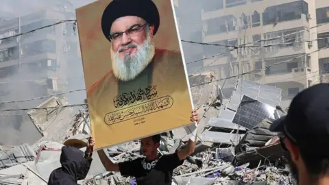 EPA A Hezbollah supporter holds a placard with Hezbollah leader Hassan Nasrallah next to the rubble of a completely destroyed building in Dahieh, a southern suburb controlled by Hezbollah, Beirut, Lebanon, 02 October 2024