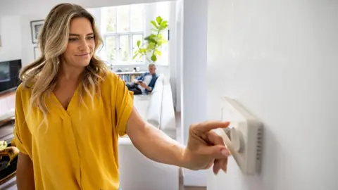 Getty Images A blonde woman adjusts the temperature of her house with a dimmer - stock photo