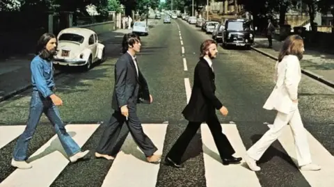 APPLE CORPS The Beatles' Abbey Road album cover shows four men, George Harrison, Paul McCartney, Ringo Starr and John Lennon, walking on a zebra crossing outside the recording studios in north London. It is a residential street with cars parked on either side of the road.