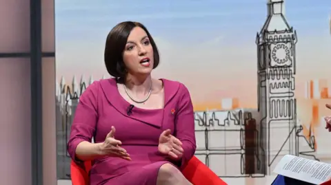 BBC Bridget Phillipson, a woman with dark hair in a bob, wearing a fuchsia pink outfit in front of a stylised graphic of the Houses of Parliament on the set of Sunday with Laura Kuenssberg 