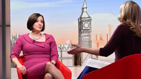 Bridget Phillipson appears on set with Laura Kuenssberg. They are both sitting on red chairs and appear to be talking. The Education Secretary wears a dark pink dress with a memorial poppy pin attached.