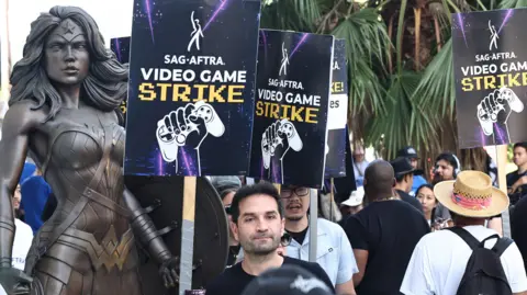 Getty Images Members of SAG-AFTRA striking at WB Studios. They're holding placards saying 