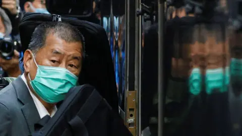 Reuters Jimmy Lai, wearing a face mask, arriving in court in 2023 