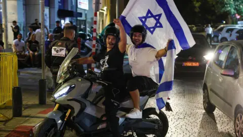 Getty Images People cheer and wave an Israeli national flags as they celebrate the news of the death of Hamas leader Yahya Sinwar, in the Israeli costal city of Netanya, on October 17, 2024. 