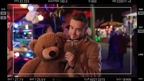 Sony Music Liam Payne, seen through the viewfinder of a film camera, poses with a teddy bear on the set of the Night Changes video in 2014