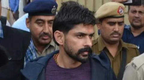 Getty Images Gangster Lawrence Bishnoi is escorted by police personnel before being produced in court on November 13, 2019 in Panchkula, India. Notorious gangsters Lawrence Bishnoi and Sampat Nehra and their aides were produced in a Panchkula district court amid tight security for framing of charges in two criminal cases that took place in 2017