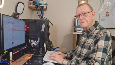 Pete Middleton Pete Middleton sitting at his computer wearing a checked shirt