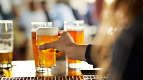 Getty Images A hand on a pint of beer at a bar.