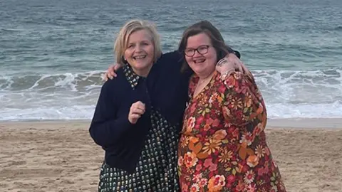 PA Media Donna Ockenden and her daughter Phoebe standing on a sandy beach with the sea behind them.