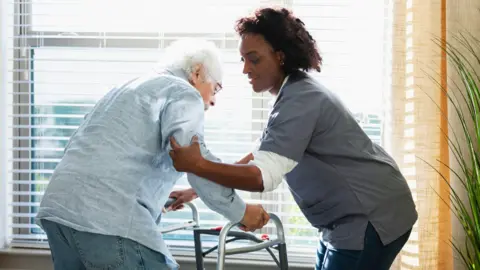 Getty Images A care home worker helps support an elderly man leaning on a walking frame