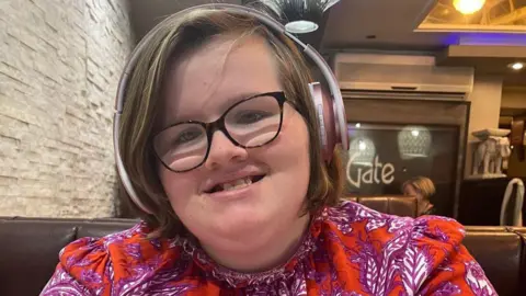 PA Media Phoebe Ockenden wearing a red floral dress and bluetooth headphones, sitting in a restaurant.