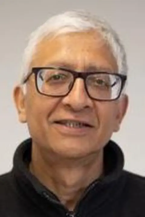 A portrait photograph of Dr Ravi Kumar who is wearing a black zip-up fleece and glasses