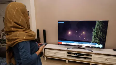 Getty Images A woman watching news of Iran's missile attack on Israel on a television in Iran