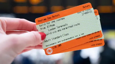 PA Media A woman with red nail varnish holding a rail ticket to from Eltham to London terminals in front of a departure board