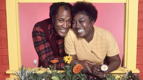 Getty Images John Amos and Esther Rolle side by side smiling through a yellow window in a publicity shot for Good Times in 1977