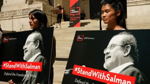 Getty Images People listen as writers gather to read selected works of British author Salman Rushdie, one week after he was stabbed while on stage, during a rally to show solidarity for free expression outside the New York Public Library in New York City on August 19, 2022. 