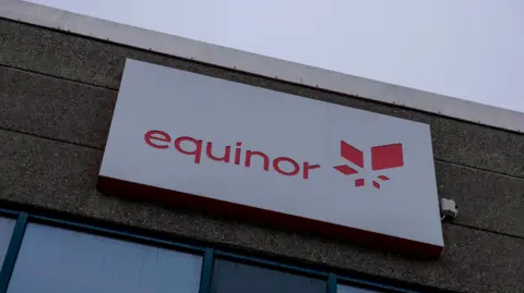 PA Media A sign for the Norwegian state oil company Equinor. The sign, on top of a dark-coloured building, is white, with the company name in red text, next to its logo, which is also in red.