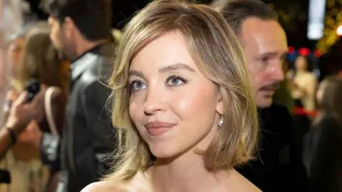 Getty Images Sydney Sweeney in a strapless dress on a red carpet. She is wearing pearl drop earrings and has her dark blonde hair in a bob.