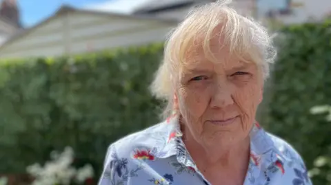 BBC Sue Robertson, a woman with grey-white hair wearing a blue short-sleeved shirt with a large floral pattern