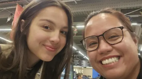 Rose Ann Bituon-Thomas US pop star Olivia Rodrigo takes a selfie with a Llandudno resident. Olivia Rodrigo is on the left and is smiling. Rose is on the right is smiling and is wearing brown framed glasses.