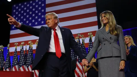 Reuters President Donald Trump points while on stage, in front of an American flag, as he holds hands with his wife Melania during his rally at the Palm Beach County Convention Center in West Palm Beach, Florida, U.S