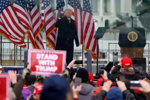 Getty Images Donald Trump raises a gloved fist to greet the crowd at a rally on January 06, 2021, in Washington, DC. One member of the crowd is holding a Stand with Trump placard.