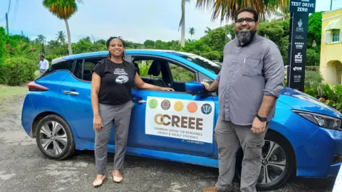 Dr Legena Henry stands next to a blue car with a sign reading 