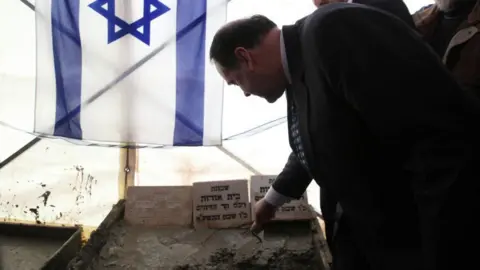 AFP Former Arkansas governor Mike Huckabee adds concrete to a corner stone in front of an Israeli flag during a dedication ceremony for a new Israeli settlement at Beit Orot, in occupied East Jerusalem on 31 January 2011.