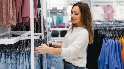 Getty Images Woman in white top looking at jeans on a rack in a clothes shop