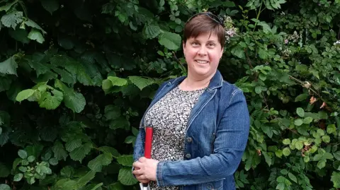 Louise Plunkett Louise Plunkett stands in front of a hedge, holding her cane.