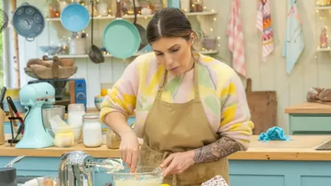 Channel 4/Love Productions/Mark Bourdillon Georgie Grasso baking in one of The Great British Bake Off tent kitchens, wearing an apron and looking serious as she concentrates