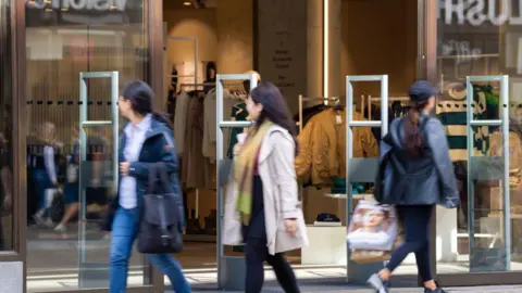 Getty Images Shoppers walk past a retail clothing store