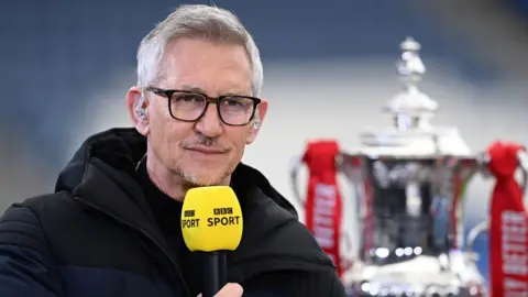 Getty Images Gary Lineker in a thick coat holding up a yellow BBC Sport microphone, with the FA Cup next to him in 2021