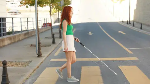 WeWalk A lady holding a cane crosses a pedestrian crossing