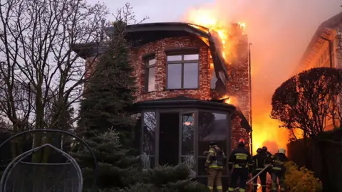 State Emergency Service of Ukraine Ukrainian Emergency Service workers stand beneath burning building as fire rages behind them