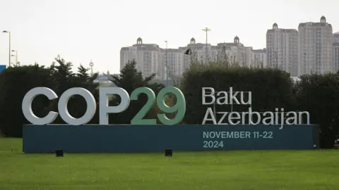 Reuters COP29 sign on a patch of grass with a backdrop of the cityscape in Baku, Azerbaijan