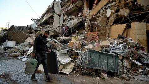 EPA A man walks past a destroyed building in the Beirut suburb of Chiyah, Lebanon, following an Israeli strike that targeted a branch of the Hezbollah-linked Al-Qard Al-Hassan financial association (21 October 2024)