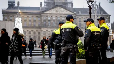 EPA-EFE/REX/Shutterstock People walk past a police car as officers stand guard on Dam Square in Amsterdam after the violence in the centre of the city the day before