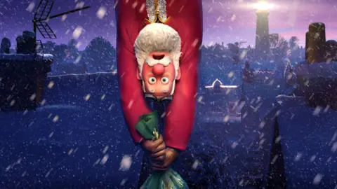 Netflix Santa Claus hanging upside down, clinging on to his sackful of presents as they dangle beneath him, in a promotional still for Netflix's That Christmas