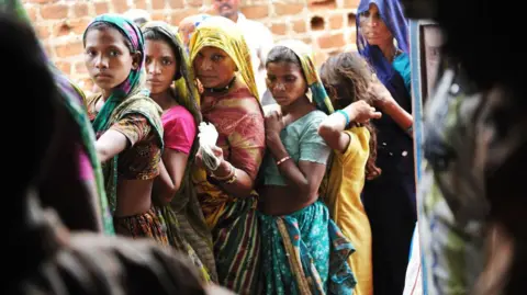 Getty Images MADHYA PRADESH, INDIA - JULY 2010: A group of Indian women line up outside the Fair Price Shop with their ration cards to receive portions of wheat, sugar, kerosene and rice from the government in Jhabua, Madhya Pradesh, India, on July 16, 2010. T